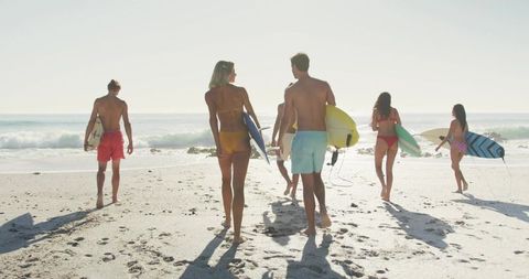 Group of Surfers Carrying Surfboards on Sunny Beach Close to Water