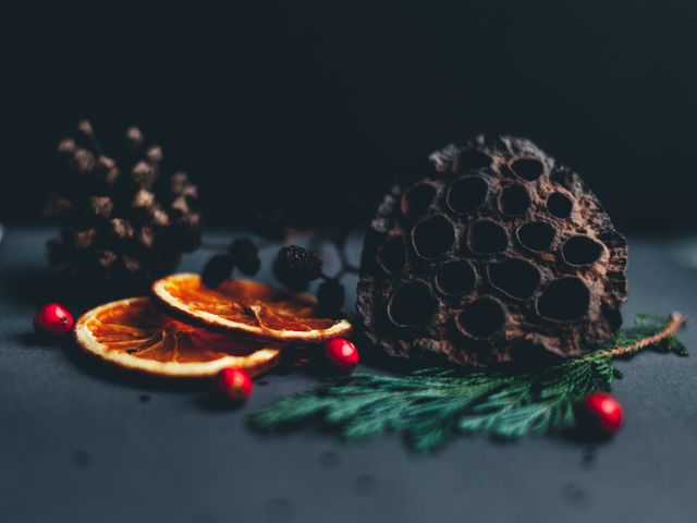 This image features a rustic winter arrangement, including dried orange slices, pine cones, and small red berries on an evergreen branch, all set against a dark background. Ideal for use in holiday cards, seasonal blog posts, or winter-themed marketing materials to evoke a cozy and festive feeling.