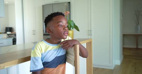 Contemplative african american boy sitting at kitchen island wearing colorful striped tee