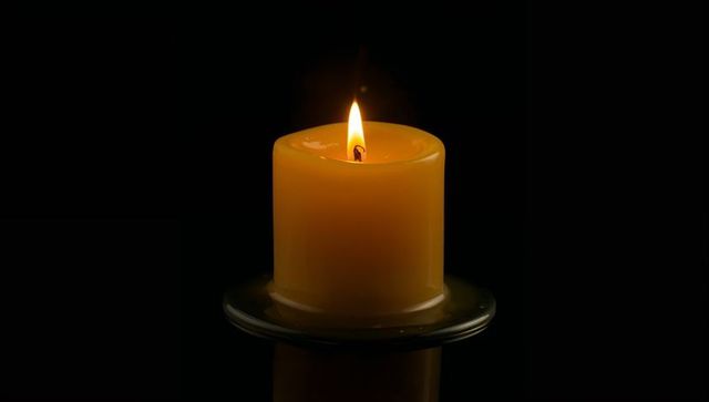 Glowing Yellow Pillar Candle Burning on Glass Holder with Melting Wax Pool and Reflection