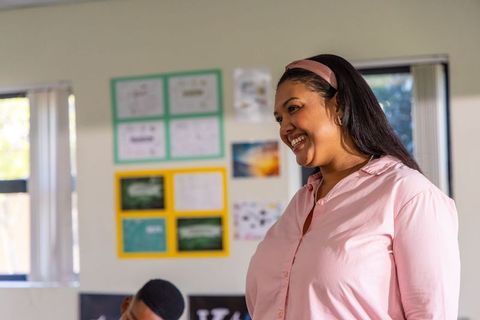 African american teacher smiling and guiding teen student in bright classroom with posters