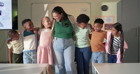 Smiling teacher embracing diverse elementary students arm-in-arm promoting teamwork