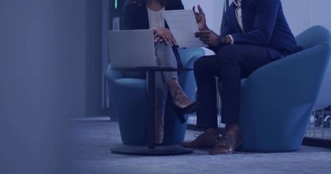 Professionals reviewing documents and laptop in modern office lounge discussing strategy