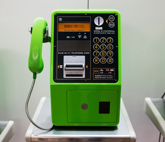 This image of a vintage green Japanese payphone with a digital display portrays a nostalgic public communication device. The bright green phone features a variety of buttons, coin inputs, and a screen displaying text. Suitable for use in projects about communications history, travel, and technological evolution.