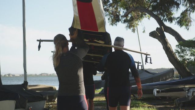 Seniors carrying a rowing boat by a lake on a clear day. Perfect depiction of teamwork, retirement activities, and outdoor fitness for older adults. Ideal for articles on active aging, community sports, or promoting healthy lifestyles for seniors.