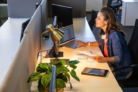 Female professional analyzing financial charts at modern open-plan desk with laptop