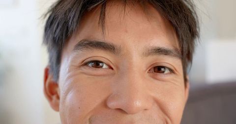 Smiling asian man holding direct gaze closeup in living room with soft natural light