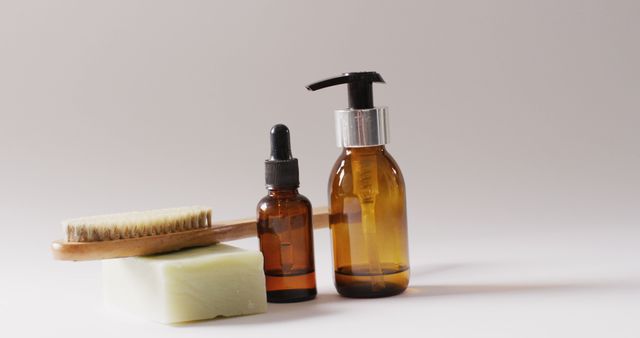 Natural skincare products including a pump bottle, dropper bottle, handmade soap, and wooden brush arranged against a plain background. Ideal for wellness blogs, product advertisements, eco-friendly lifestyle promotions, and skincare routines.