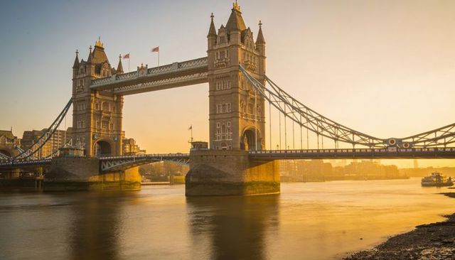Golden-hour tower bridge over river thames with reflection and passing tour boat