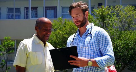 Doctor and senior man reviewing medical report outdoors