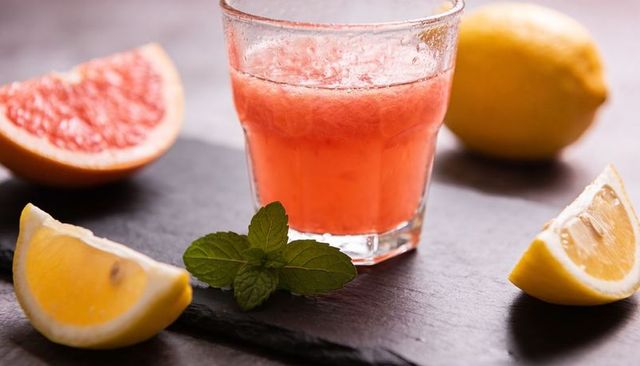 Refreshing pink grapefruit lemonade featuring fresh mint and lemon wedges on dark slate