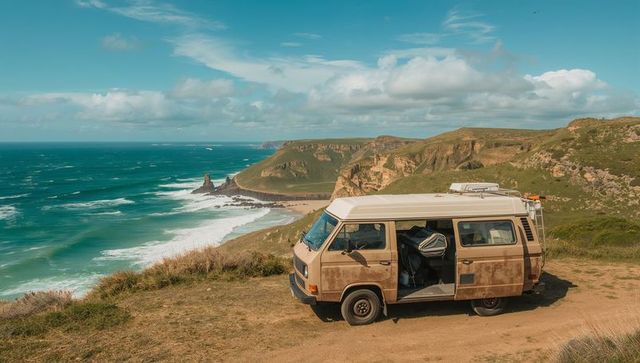 Vintage camper van sitting on coastal cliff overlooking turquoise ocean waves