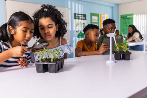 Elementary students examining seedlings with magnifying glass and tablet in stem lab