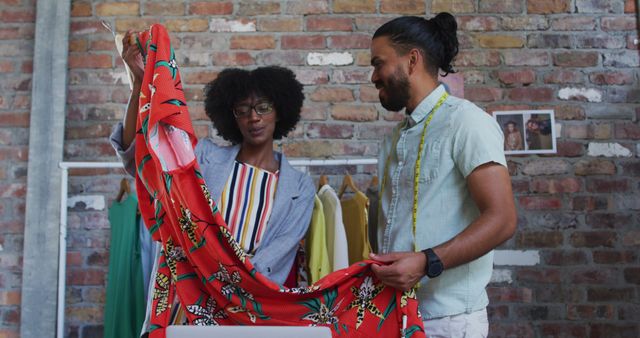 Depicts two fashion designers in a creative workspace collaborating on a vibrant red dress design. Suitable for design, teamwork, textile, fashion industry, and collaboration themes. Useful for blogs, articles, and marketing materials highlighting fashion design process or creative teamwork.