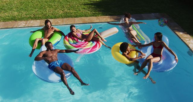 Group of diverse friends enjoying a sunny day on colorful pool floats in backyard pool. Perfect for ads about summer fun, leisure activities, pool parties, and outdoor entertainment. Great visual for promoting swimwear, pool accessories, and summer events.