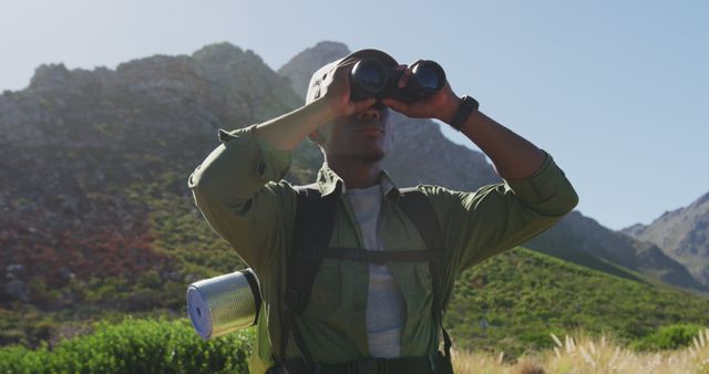 African american man hiking in mountain countryside using binoculars. fitness training and healthy outdoor lifestyle.