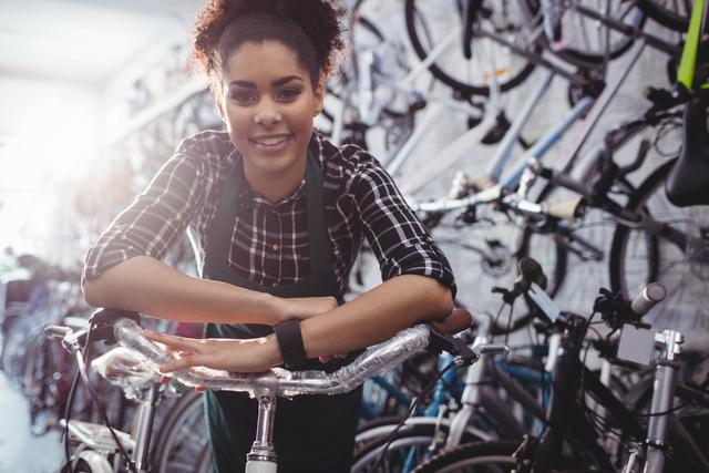 Young female bicycle mechanic smiling confidently while leaning on a bike in a repair workshop. Ideal for articles about empowering women in skilled trades, promoting small businesses, or illustrating passion for cycling and bike maintenance.