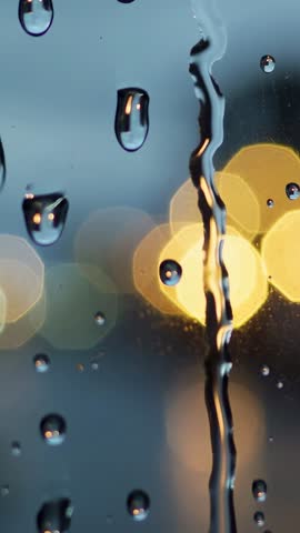 Vertical video Detaching droplet sliding down wet window at dusk with bokeh lights
