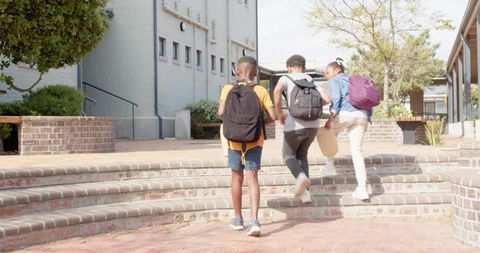 Diverse School Friends Climbing Steps into Courtyard With Backpacks