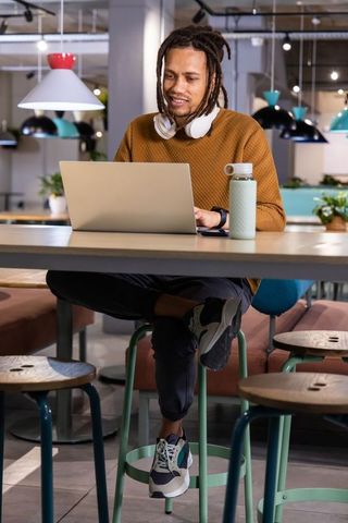 African american freelancer working on laptop in modern coworking cafe with headphones