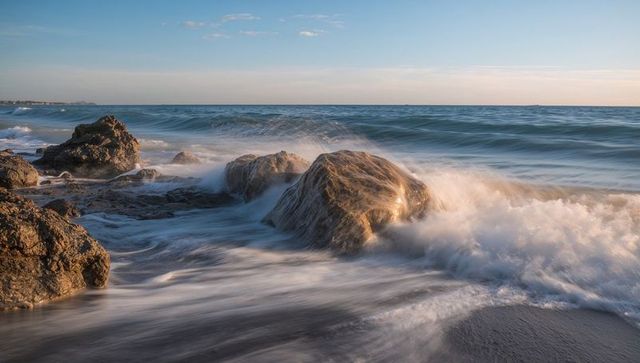 Breaking waves washing over sunlit coastal boulders during golden hour