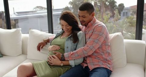 Couple embracing parenthood on cozy sofa in sunlit room