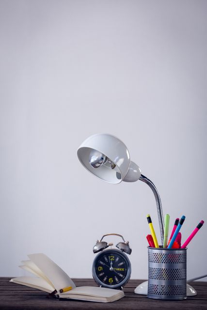 Electric lamp with desk organizer by book and alarm clock on table against wall