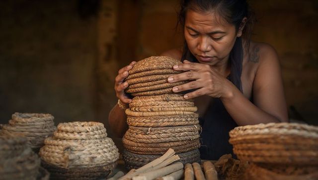 Artisan arranging coiled handmade baskets and natural fibers in rustic weaving workshop