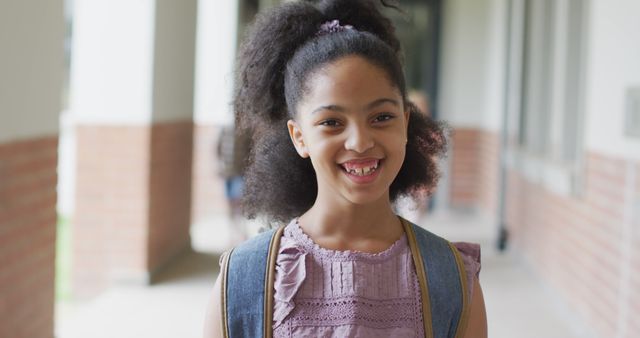 Image of happy biracial girl standing at school corridor. primary school education and learning concept.