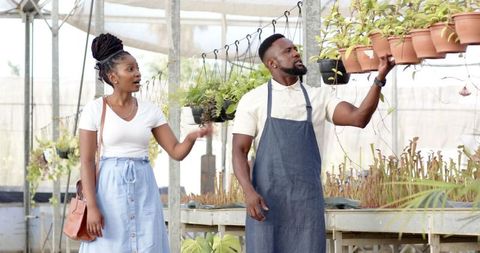 Nursery employee assisting customer in greenhouse horticulture scene