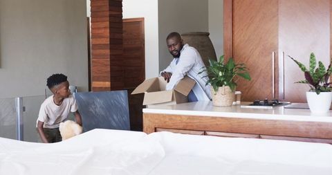 African American Father and Son Packing Boxes in Modern Kitchen During Move