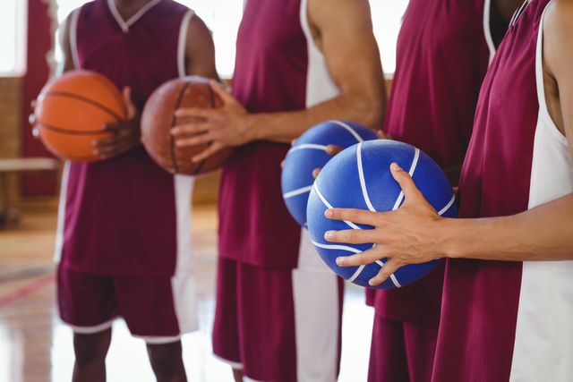 Basketball players in maroon and white uniforms holding basketballs in a gymnasium. Ideal for use in sports-related content, team-building articles, fitness and training materials, and promotional content for basketball events or athletic programs.