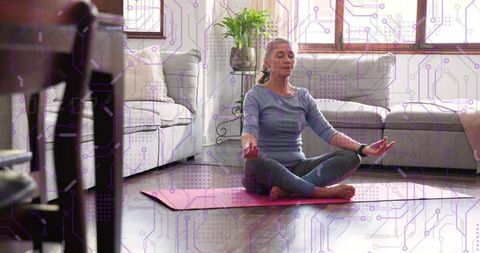 Mature woman meditating in living room on pink yoga mat with digital wellness overlay