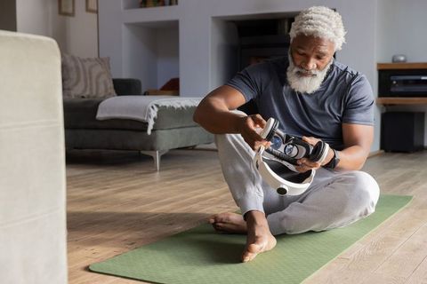 Senior african american man adjusting vr headset while sitting on green mat in living room