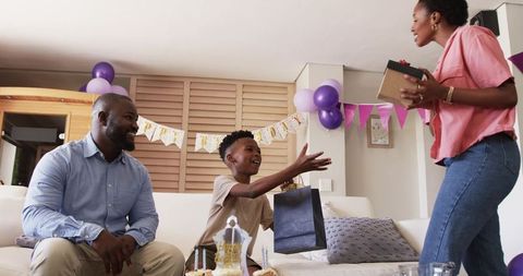 African American family celebrating birthday at home with child reaching for gift bag