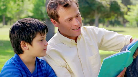 Father Reading Book with Son Outdoors