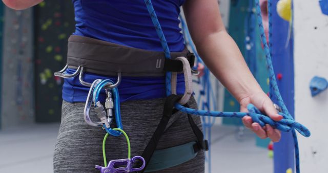 Midsection of caucasian woman knotting rope in a harness belt at indoor climbing wall. fitness and leisure time.