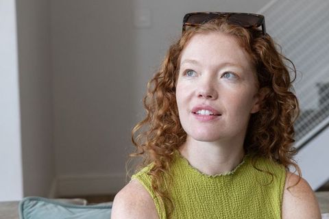 Relaxed red-haired woman sitting on couch wearing green knitted top and sunglasses