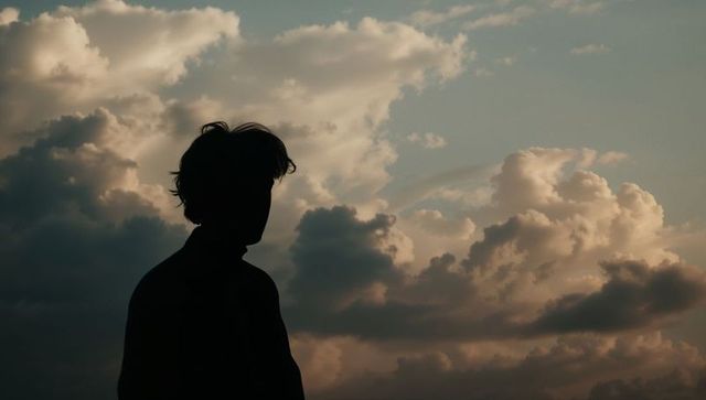 Silhouette of Teen at Sunset Amidst Peaceful Cloudscape