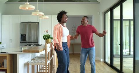 African american couple dancing and laughing in modern open-plan kitchen sharing joy