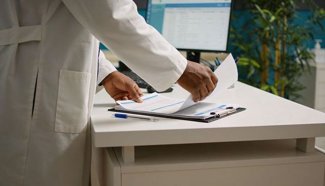 Clinician reviewing records and patient documents at clinic reception with clipboard