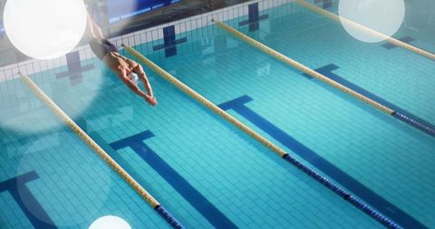 Competitive swimmer diving into indoor pool lane at race start under bright lights