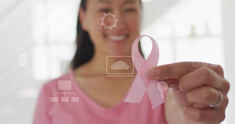 Holding pink breast cancer ribbon, smiling Korean woman wearing pink shirt and ring, tech icons over