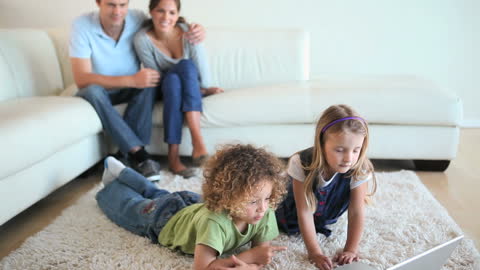 Children Playing on Laptop with Parents Relaxing in Background