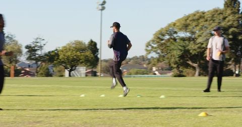 Athlete performing cone agility drill on field while coach guiding sprint and hop training