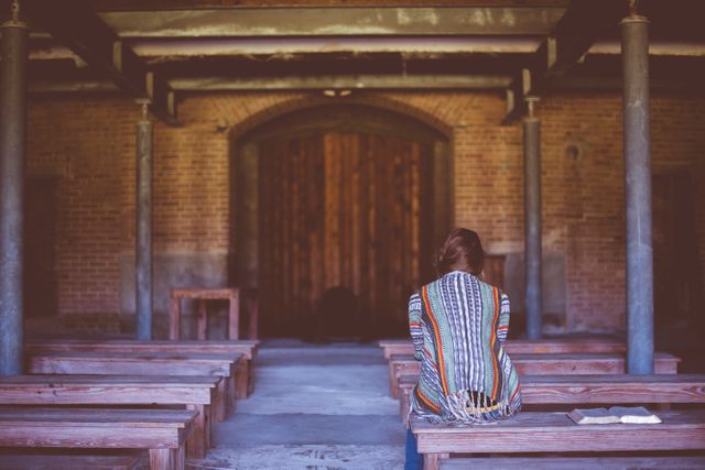 Individual sitting alone in silent, rustic church interior with wooden benches. Perfect for themes related to solitude, spirituality, meditation, and contemplative moments. Ideal for use in religion-oriented content, mental health resources, and peaceful, introspective scenes.