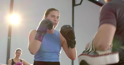 Woman boxer practicing focused punches while coach holds mitts during intense gym training