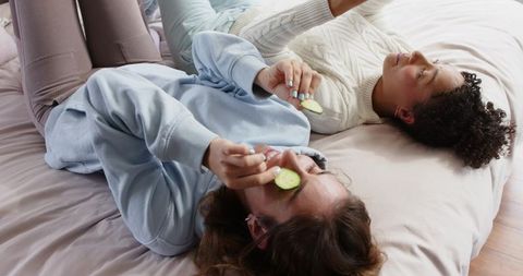 Diverse friends relaxing with cucumber eye slices on bed in cozy at-home skincare moment