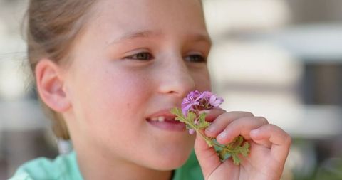 Young girl smelling pink blossoms on porch closeup capturing childhood curiosity and calm