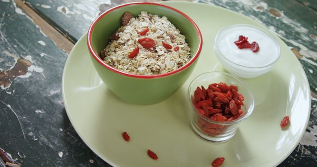 Nutritious breakfast bowl with oats and goji berries, accompanied by a small glass of yogurt and additional goji berries on rustic wooden table. Ideal for promoting health and nutrition-related content, balanced diet, organic food blogs, and breakfast recipes.